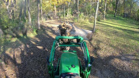 High-angle-point-of-view-on-small-green-tractor-using-lift-forks-to-move-a-tree-stump