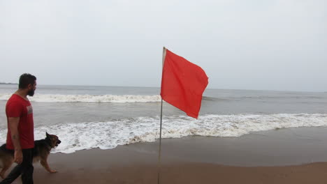 Perro-Pastor-Alemán-En-La-Playa-Jugando-Con-Su-Dueño-Cerca-De-La-Señal-De-Advertencia-De-Bandera-Roja-|-Alerta-Alta-De-Advertencia-De-Bandera-Roja-En-La-Playa