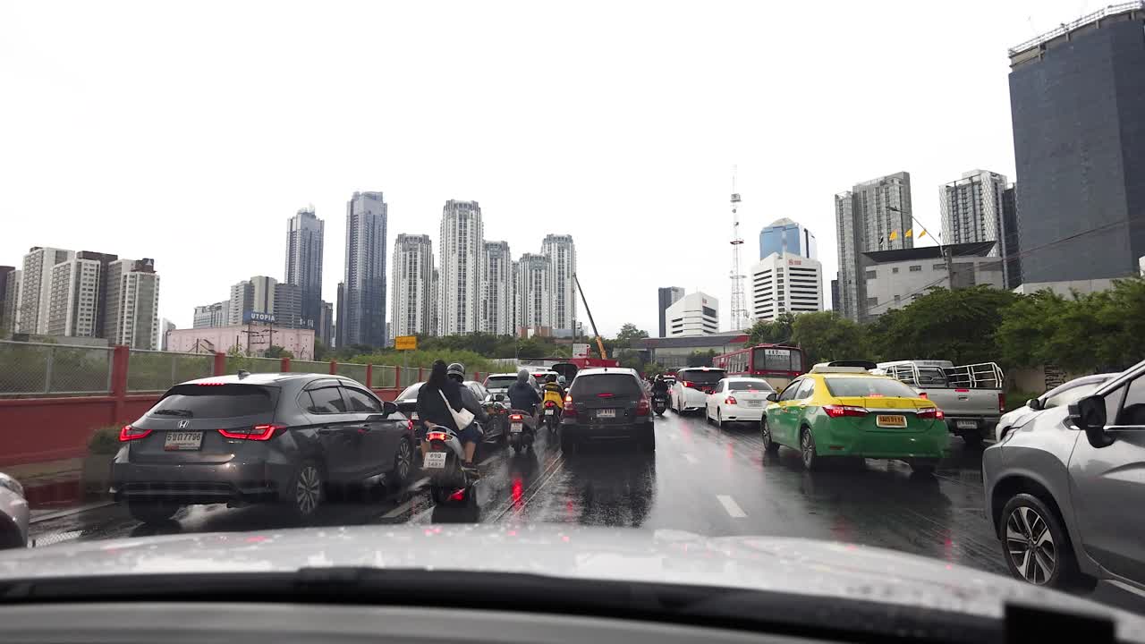 Motorcycles navigate congested cars on wet Bangkok street, overcast daylight, urban skyline background