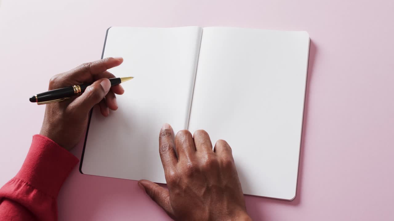 Close up of hands holding pen and blank pages of book, copy space on pink background, slow motion