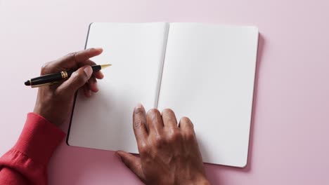 close up of hands holding pen and blank pages of book, copy space on pink background, slow motion