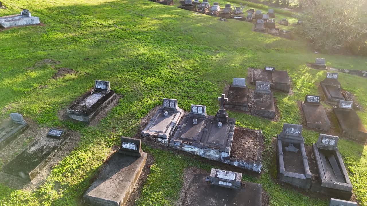 Drone footage captures a serene cemetery landscape with rows of gravestones under warm, golden sunlight