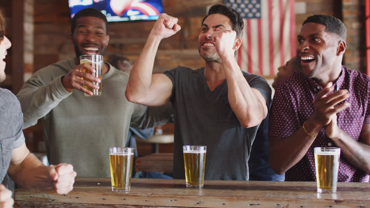 grupo de amigos masculinos celebrando mientras ven el juego en la pantalla en un bar deportivo