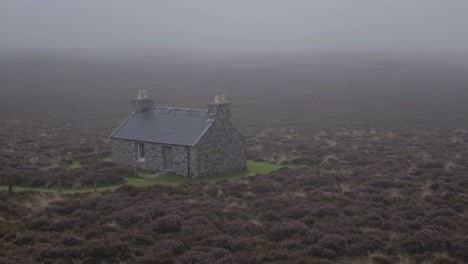 misty moorland landscape revealing weathered stone cottage, heather covered ground emerging through swirling morning fog, creating ethereal pastoral scene