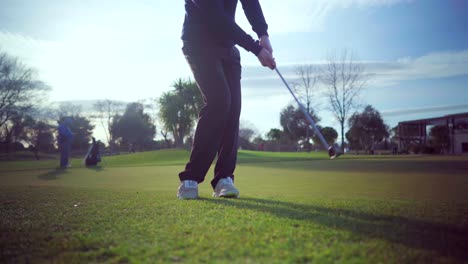 swing shot of a golfer on the approach green of a golf course, on a sunny day