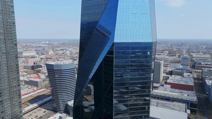 Vista elevata della città di un alto grattacielo di vetro blu centrato tra torri per uffici, densi edifici urbani e un ampio skyline sotto la chiara luce del giorno