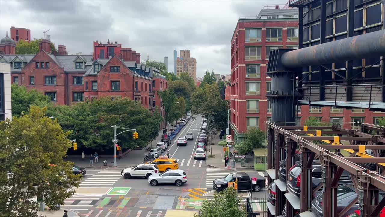 Iconic yellow cabs and traffic drive along New York City street in Hudson neighborhood, static shot from The High Line public park
