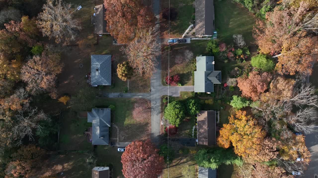 Smooth aerial drone flight over a tree-lined American suburb, capturing houses and winding roads amid fall foliage, suggesting peaceful living and subtle digital connectivity