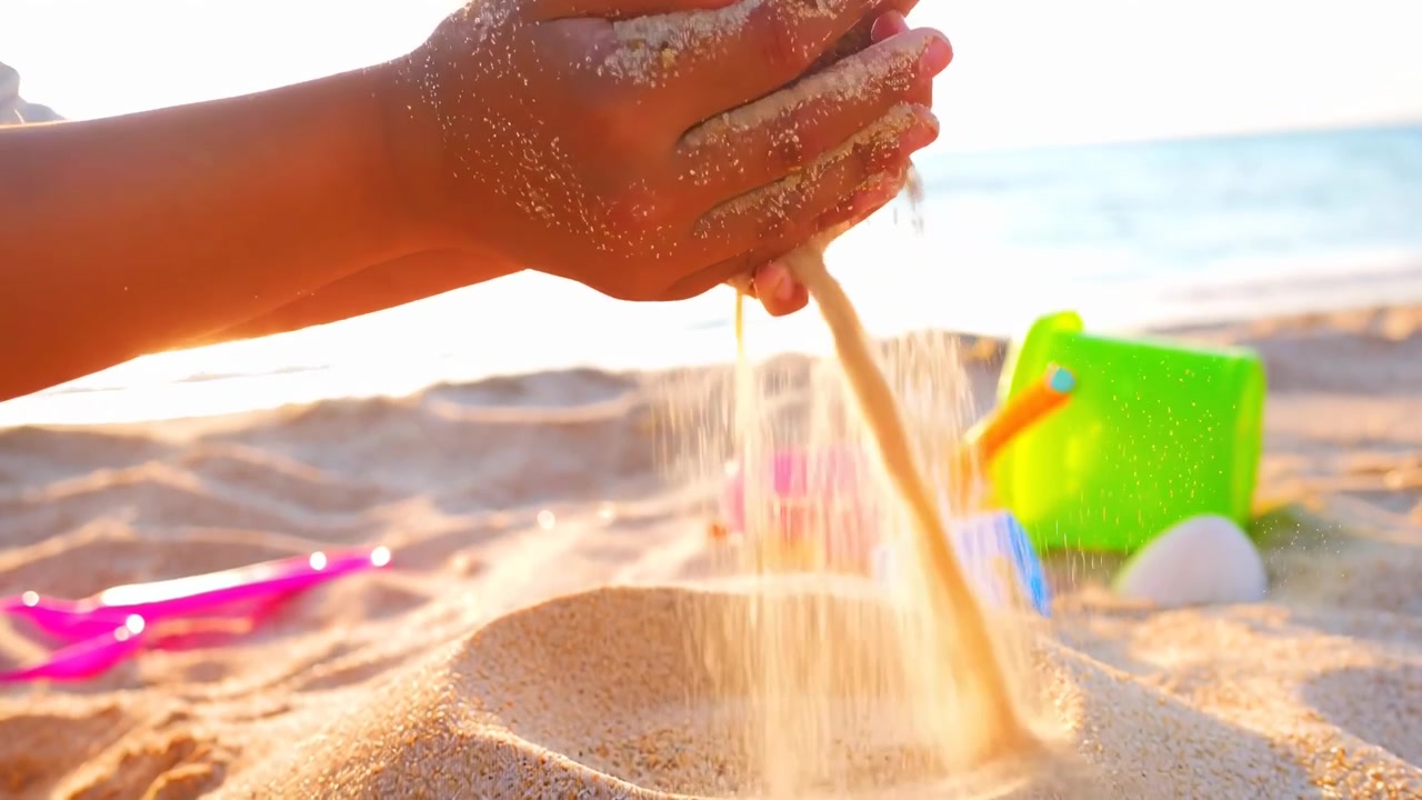 Barnhänder som siktar gyllene sand på en solig strand vid solnedgången