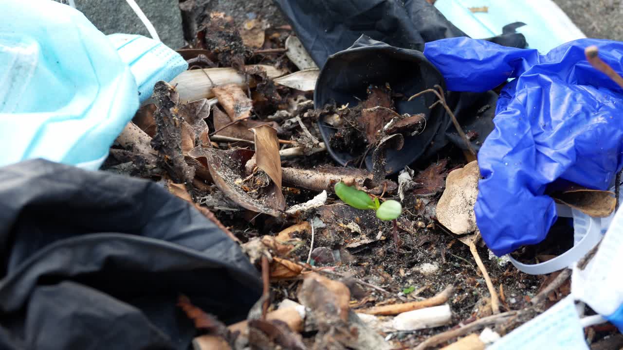 máscaras faciales desechables sucias y desagradables del virus de la corona y guantes de látex entre los residuos de basura de cigarrillos en la acera de la calle empuje en primer plano