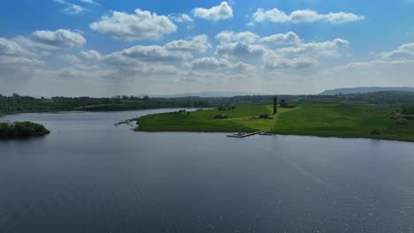 devenish island, county fermanagh, northern ireland, june 2023. drone pushes forward over the sparkling lower lough erne water towards the 12th century round tower and ruined abbey on a sunny day.