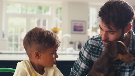 padre con perro mascota en casa en la cocina ayudando a su hijo con la tarea