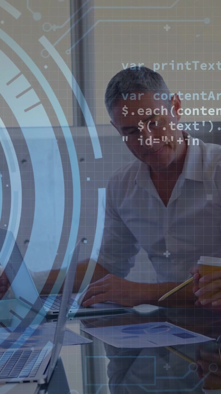 Vertical video: Man typing and following peer pointing at charts HUD code overlaying IT analysis