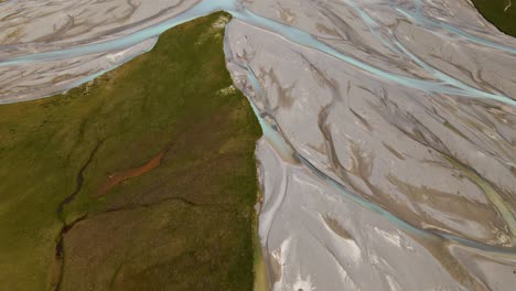 aerial shot revealing epic snow-capped mountain range behind a glacier river delta with turquoise water feeding lake tekapo