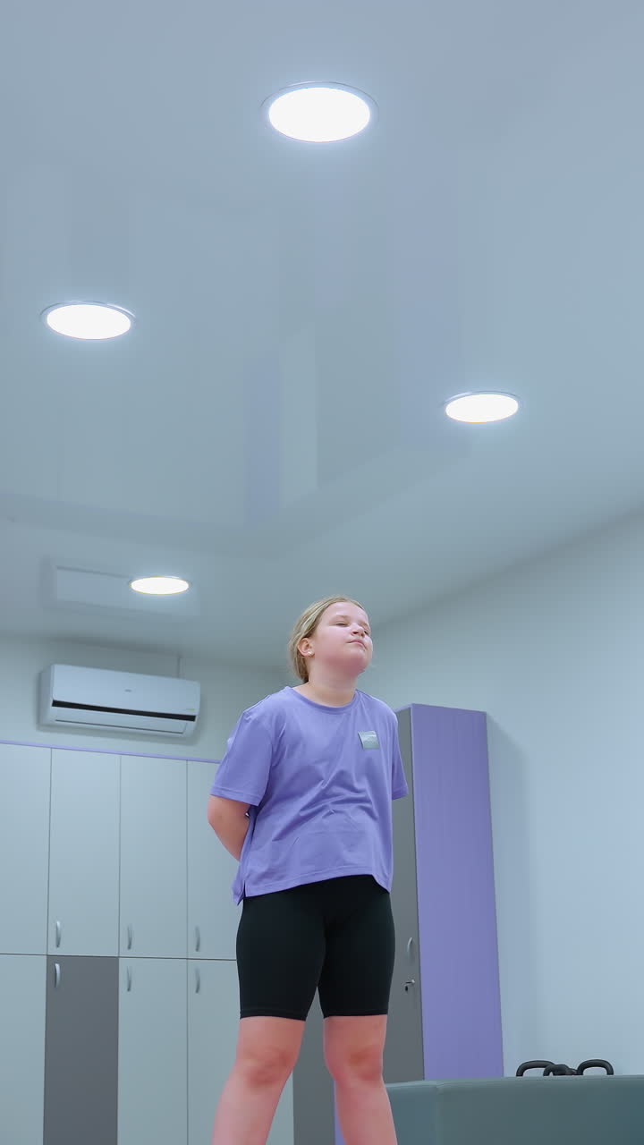 grupo de niños en un gimnasio participando en una sesión de entrenamiento, estirando los brazos hacia adelante con enfoque, el fondo presenta equipos de fitness, casilleros y bolas de ejercicio