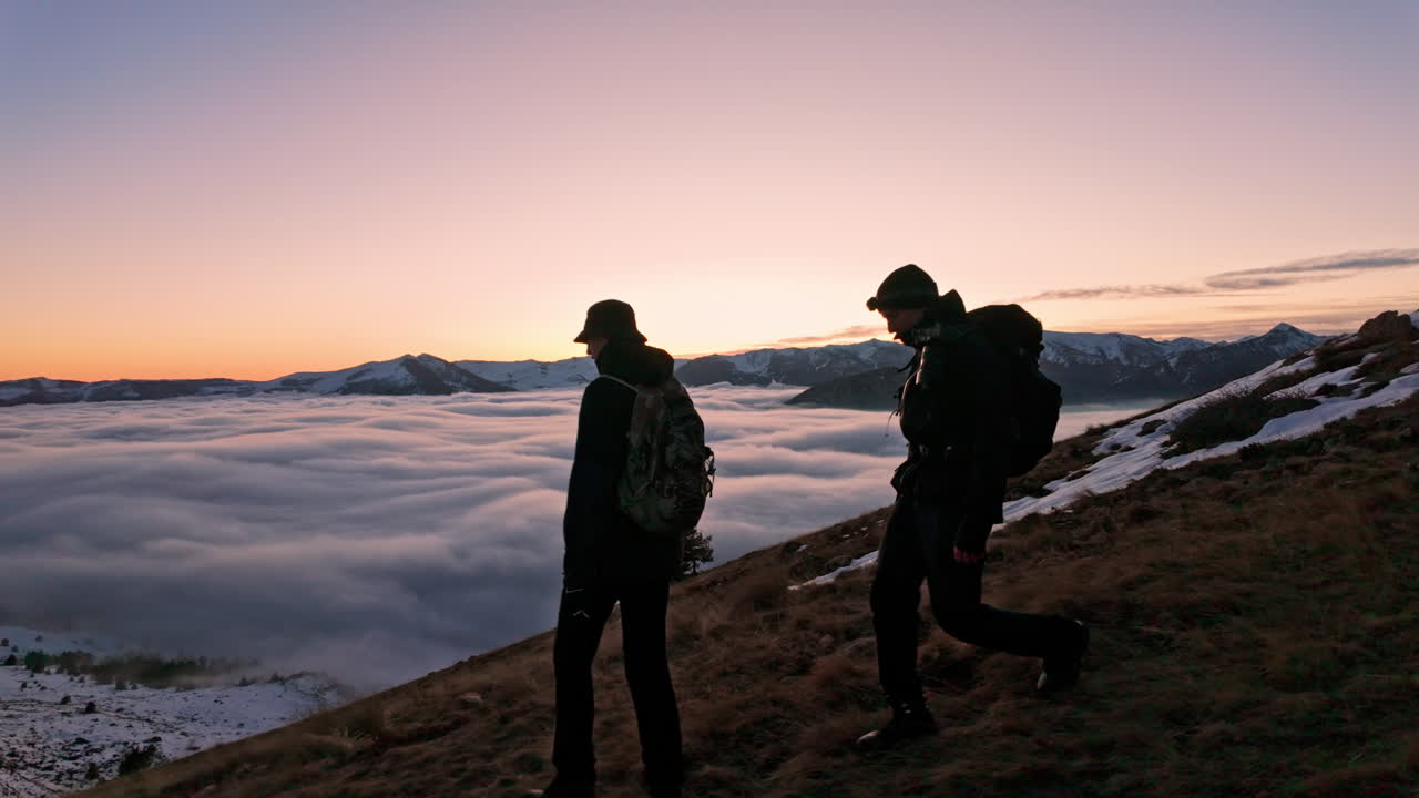 Two hikers at dawn overlook vast clouds in the mountain landscape