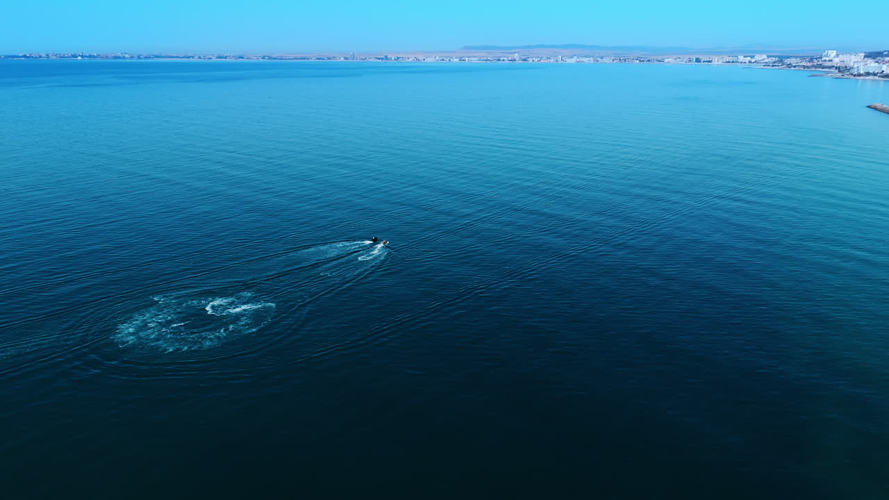 Vast blue waterscape of the sea from aerial perspective. Two people ride the jet ski scooters