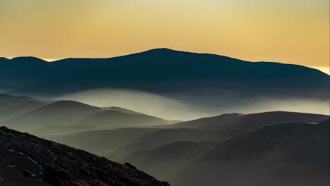 Colorida-Puesta-De-Sol-Sobre-Una-Cadena-Montañosa-Con-Niebla-Que-Se-Construye-Lentamente-En-La-Base-De-La-Montaña,-Cielo-Naranja,-Rumania