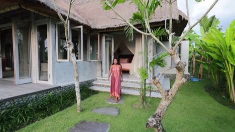 young asian woman walking outside to a garden from a bohemian tropical villa in bali