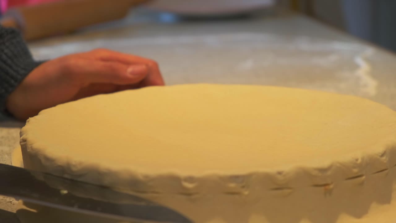 Close up of cook delicately trims excess dough from the pie tray using a knife. Each movement is slow and precise, showing care in the final steps of preparation.