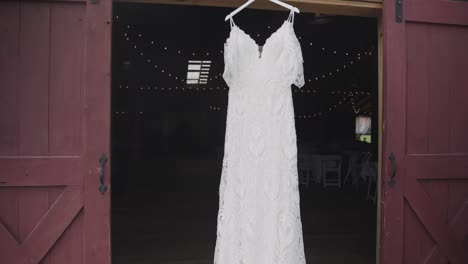 white wedding gown hanging between rustic barn doors before ceremony celebration