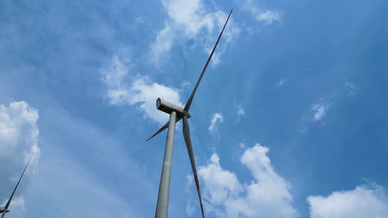 Low-angle view of modern wind turbine under blue sky with scattered clouds, clean technology and sustainable innovation
