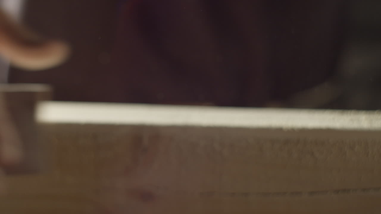 High quality video showing a craftsman sanding a wooden board in warm light with slow smooth hand movements and fine dust in the air creating a rich tactile workshop atmosphere