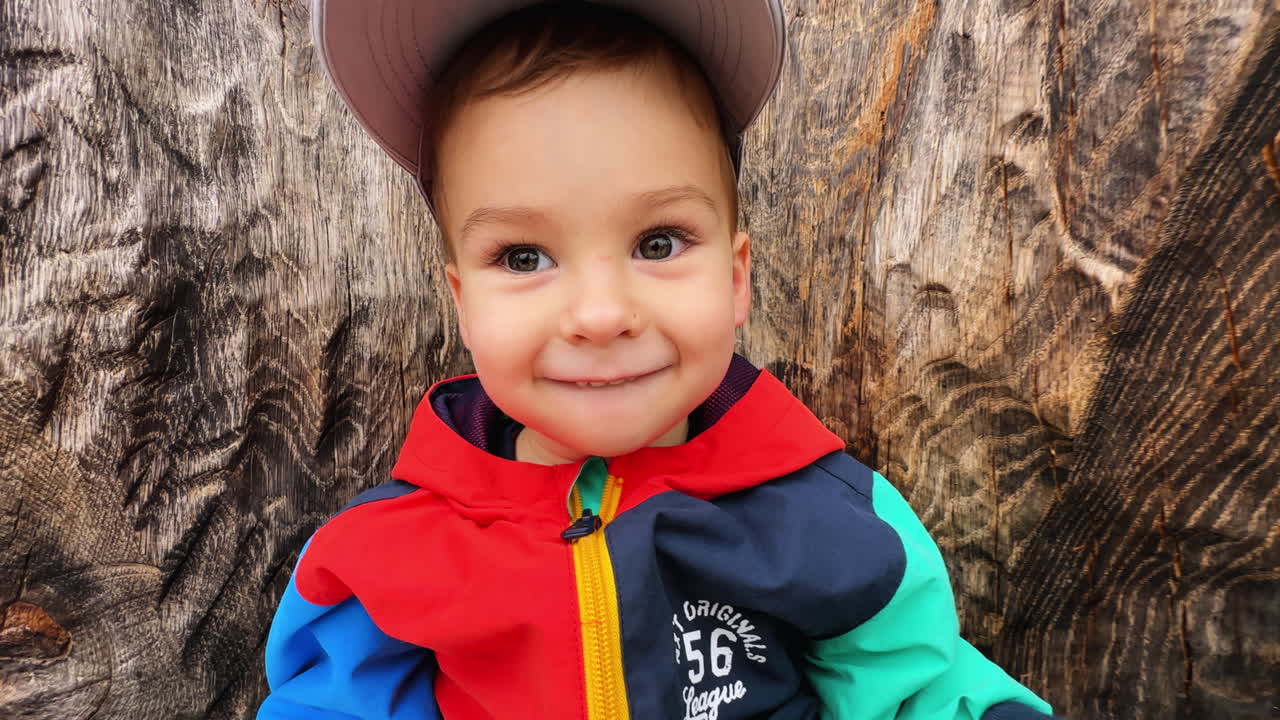 Happy thoughtful baby boy sitting on the wooden sculpture. Cute toddler holding a book in hands.