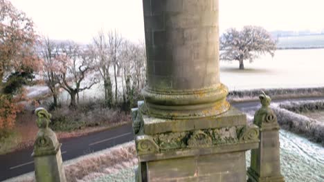 Full-Rising-drone-shot-of-the-monument-at-Castle-Howard-showing-whole-obelisk-from-bottom-to-top-on-snowy-and-frosty-winter-day