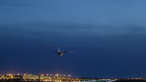 small propeller plane flying against blue hour sky, landing on airport runway