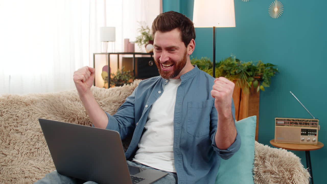 Young man happily clapping hands in front of laptop celebrating good news or online competition win