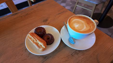 shot of a cup of coffee and freshly baked eclair and buns on a wooden table in the local cafeteria