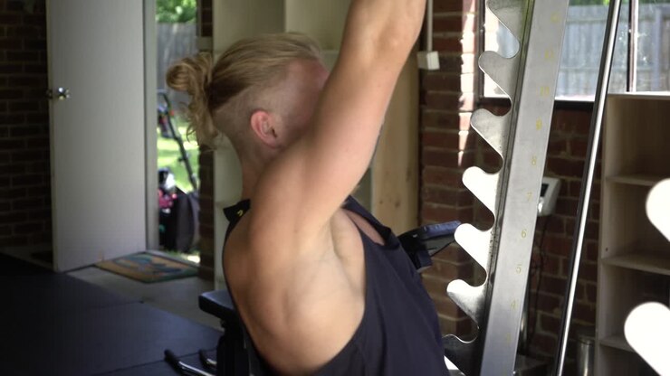 Tattoo man muscles in home gym doing close grip lat pulldowns shot from side