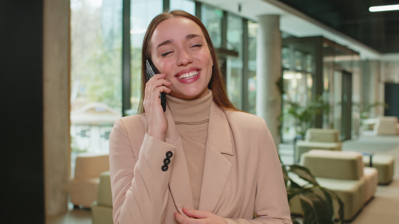 미소 짓는 백인 젊은 사업가 여성이 스마트폰으로 얘기하고 사무실 호텔 로비에서 일에 대해 논의하고 있습니다.