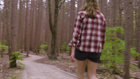 sweeping handheld shot of a young woman walking along a path in the woods