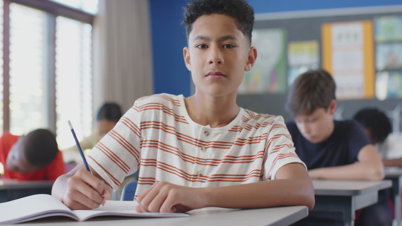 In school, boy writing in notebook while classmates studying in background