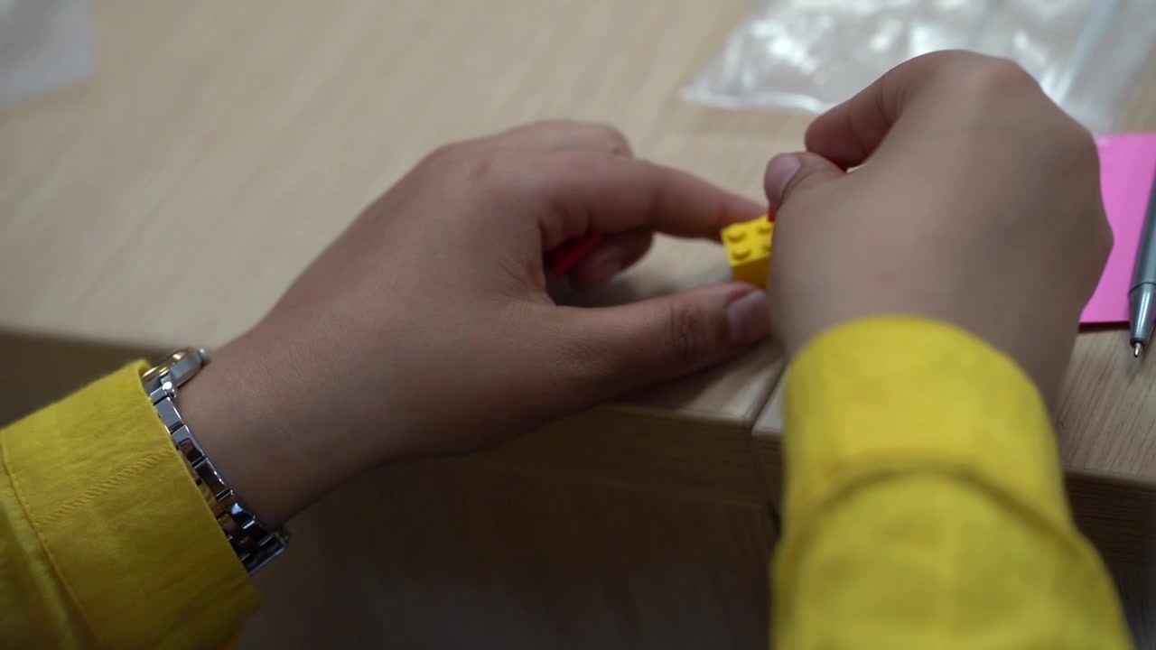 Behind head of Caucasian woman pan right to reveal her hands assembling interlocking plastic bricks, close up slow motion