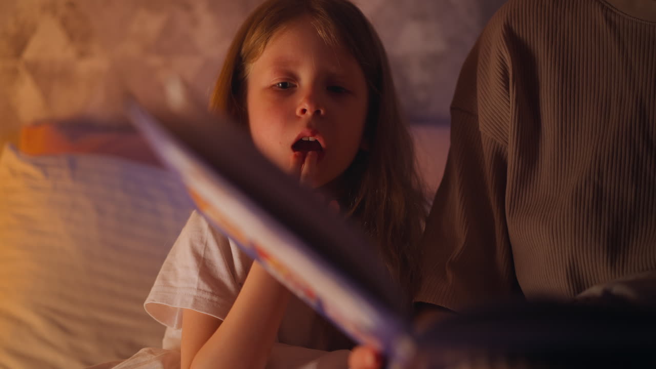 소녀는 입에 손가락을 넣고 어머니는 침대에서 손을  ⁇ 습니다.