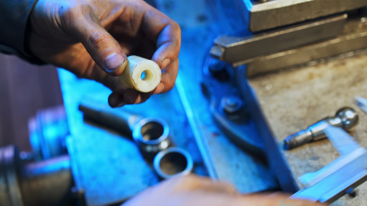 Dirty hands of a turner measuring the plastic piece with the help of calipers. Close up. Metal lathe background in blur.