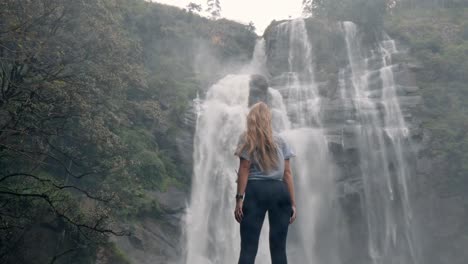 a woman stands in awe before the roaring bomburu ella waterfalls, surrounded by mist, jungle, and rocky cliffs in the lush highlands of nuwara eliya, sri lanka.