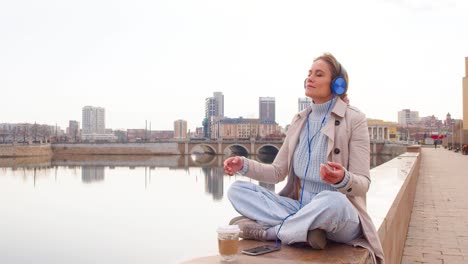 a young woman meditates on the embankment. she sits in headphones and listens to relaxing music. rest from office bustle and city noise
