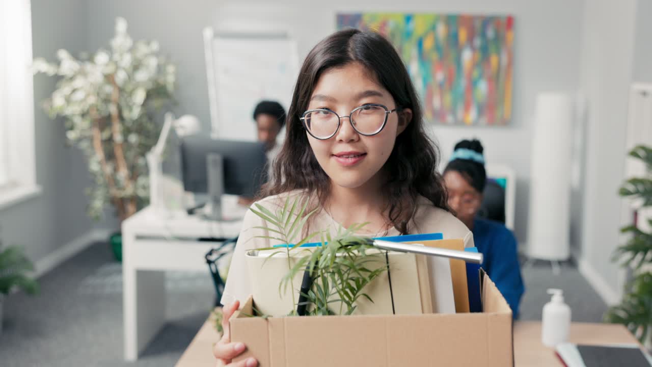 멋진 옷과 안경을 입은 여성, 야심 찬 직원이 사무실을 떠나고, 위치를 바꾸고, 다른 책상으로 이동하고, 카드보드 상자에 포장된 액세서리를 들고, 작별 인사, 미소, 만족