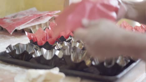 a pastry chef places red liners into a baking tray, preparing to bake muffins or cupcakes