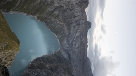 Day-to-night-sunset-time-lapse-above-lake-Limmernsee-in-Linthal-of-canton-Glarus,-Switzerland-with-stars-and-moon-appearing-in-the-sky-above-the-turquoise-waters-in-between-the-cliffs