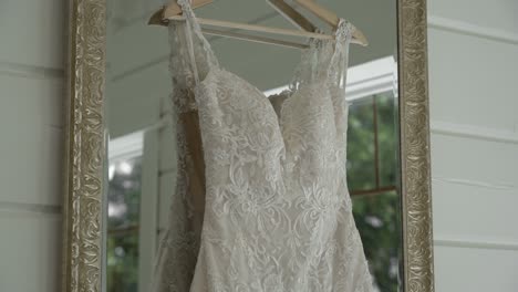 gorgeous pan of a white wedding dress hanging in a mirror which is reflecting the image of the woods outside teh window in a well lit white room at le belvédère in wakefield, quebec, canada