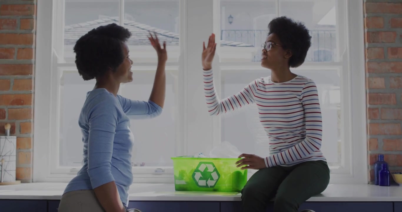 Mom and teen sorting into green bin in kitchen, light streaks swirling around hands, high-fiving
