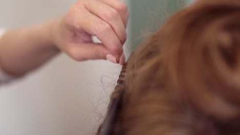 close up shot of a red headed woman getting her hairs curled in the studio. hairdressed uses curling iron. unrecognizable