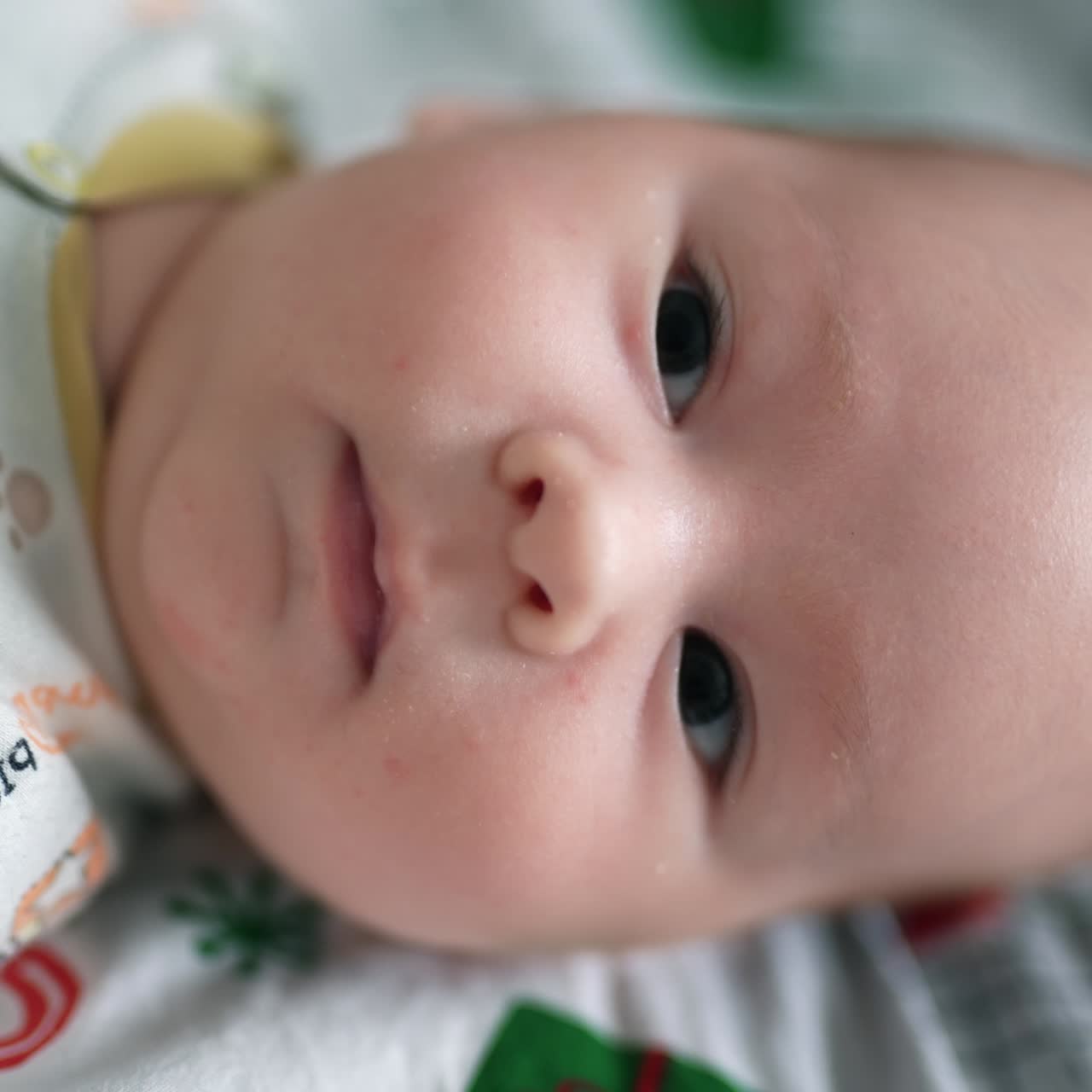 Cheerful active little kid staying active when lying on the bed. Beautiful baby face looking into camera close up. Blurred background