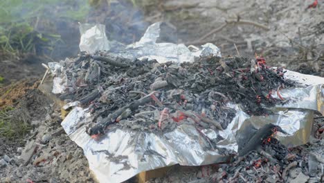 Close-up-shot-shoveling-hot-coals-onto-foil-on-a-make-shift-backyard-oven