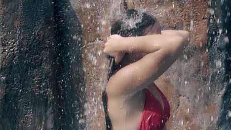 chica en bikini rojo se encuentra bajo los arroyos de agua que caen
